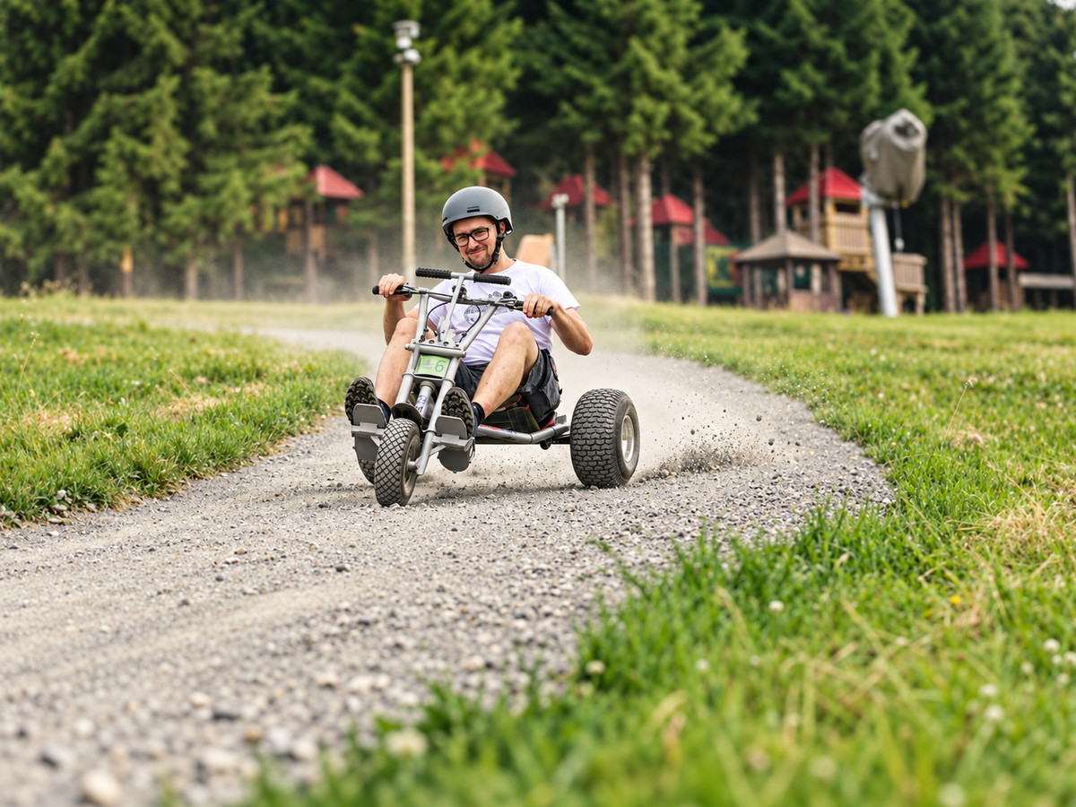Eine Person, die einen Aktivurlaub genießt, fährt mit einem Go-Kart im Dreirad-Stil zügig um eine Kurve auf einem Schotterweg, im Hintergrund sind grünes Gras und Bäume zu sehen.