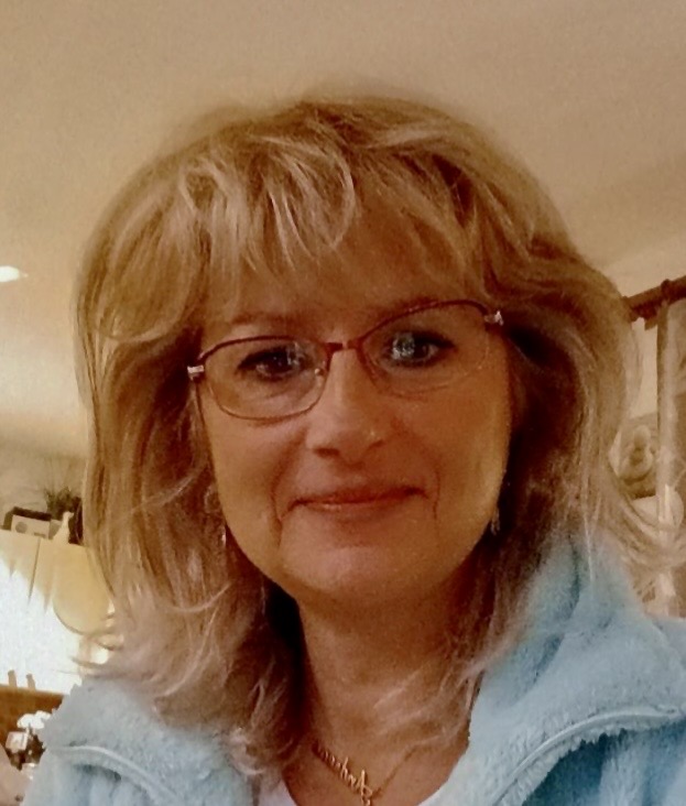 Das Porträt einer Frau mit blonden Haaren, die eine Brille und ein blaues Oberteil trägt.