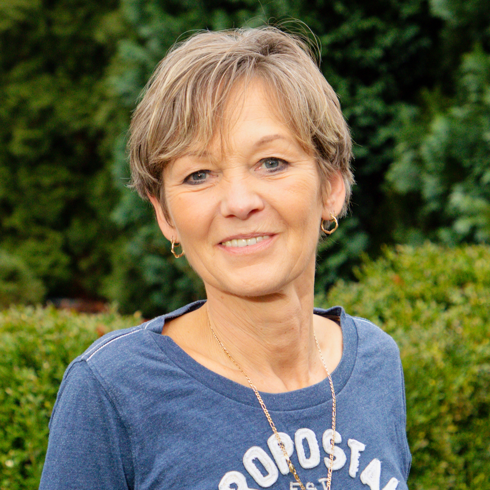 Eine lächelnde Frau mit kurzen, hellbraunen Haaren, die im Freien posiert.